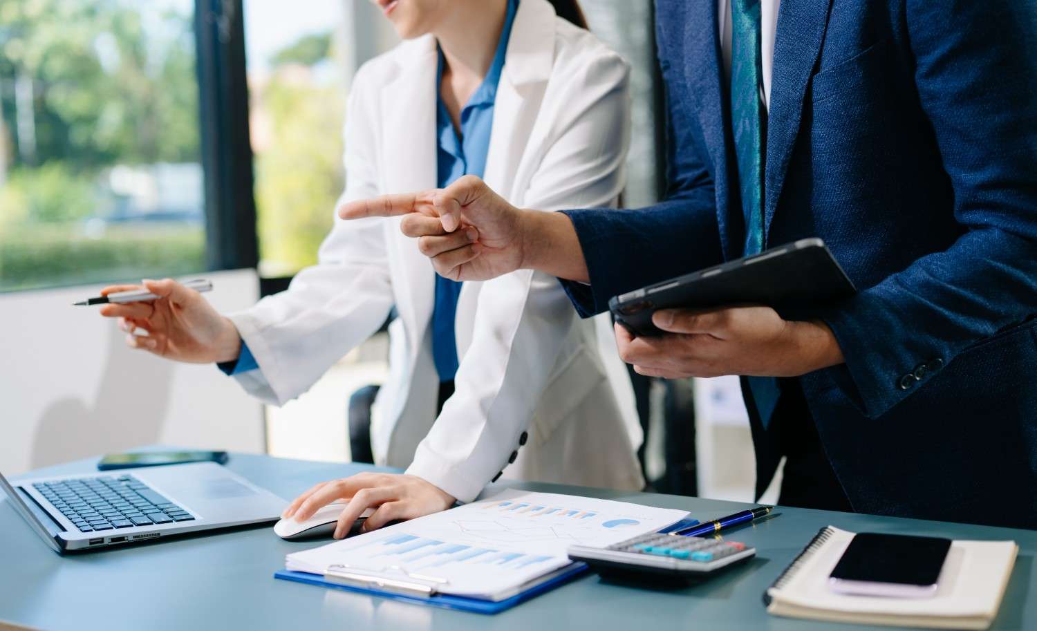 Healthcare professionals reviewing hospital procurement and purchased services cost analysis on a laptop and tablet.